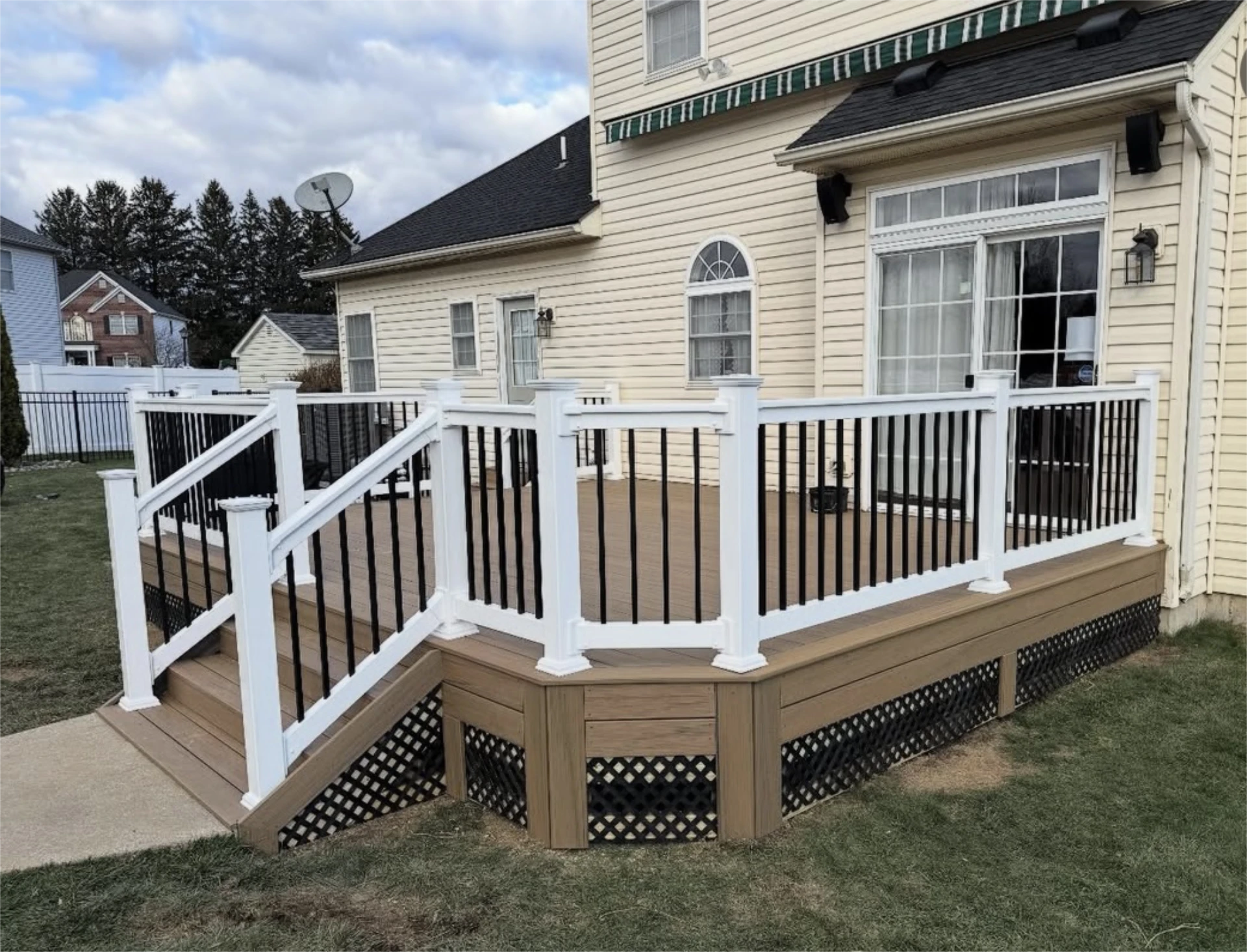 Backyard composite deck with stairs, white posts, and black balusters attached to a beige house.
