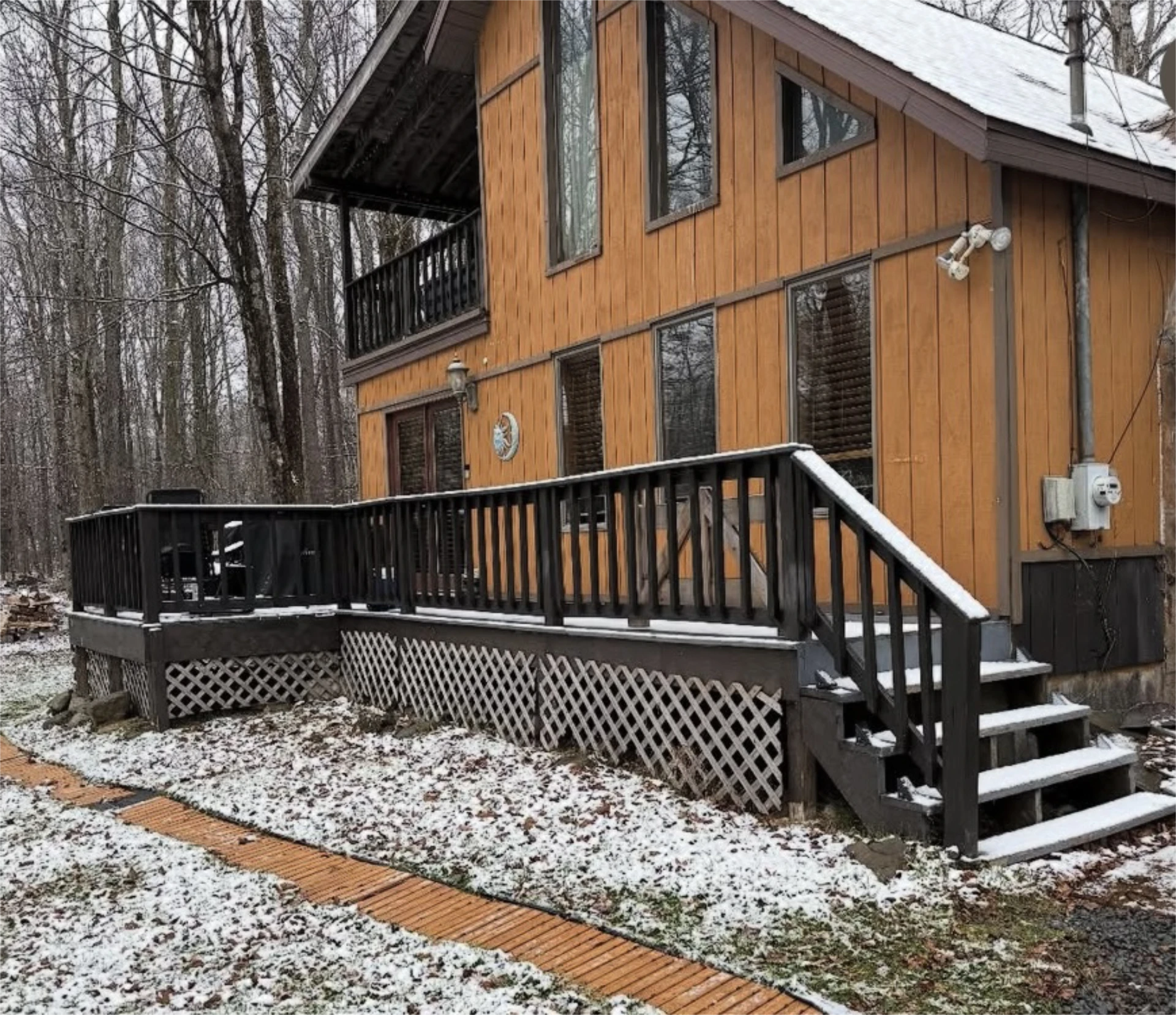 Black deck and stairs on wooded cabin with light snow.