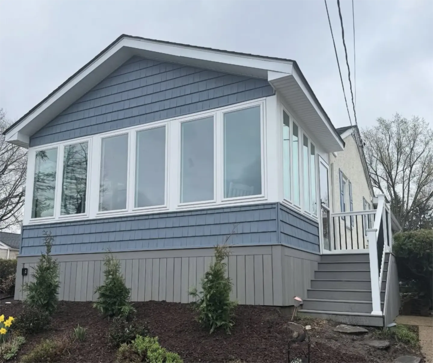 Blue sunroom addition with large windows and front steps.