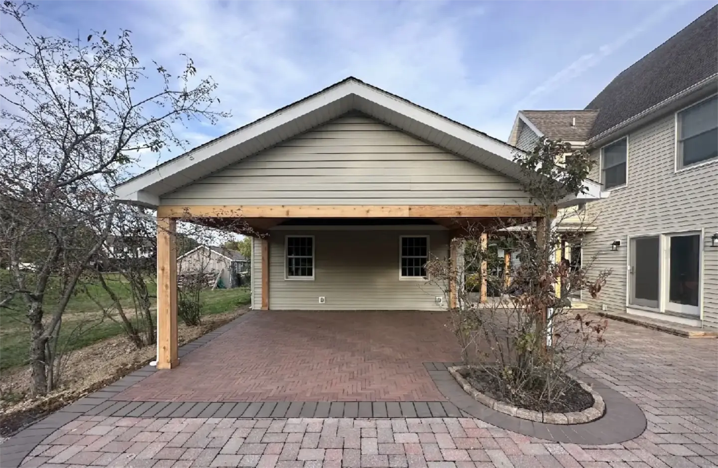Covered backyard pavilion with wood posts and brick paver patio beside a house.