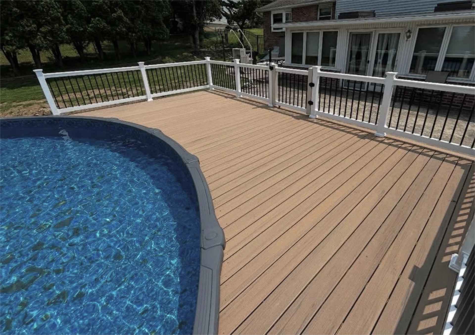 Curved edge of above ground pool next to wide composite deck and gated railing area.