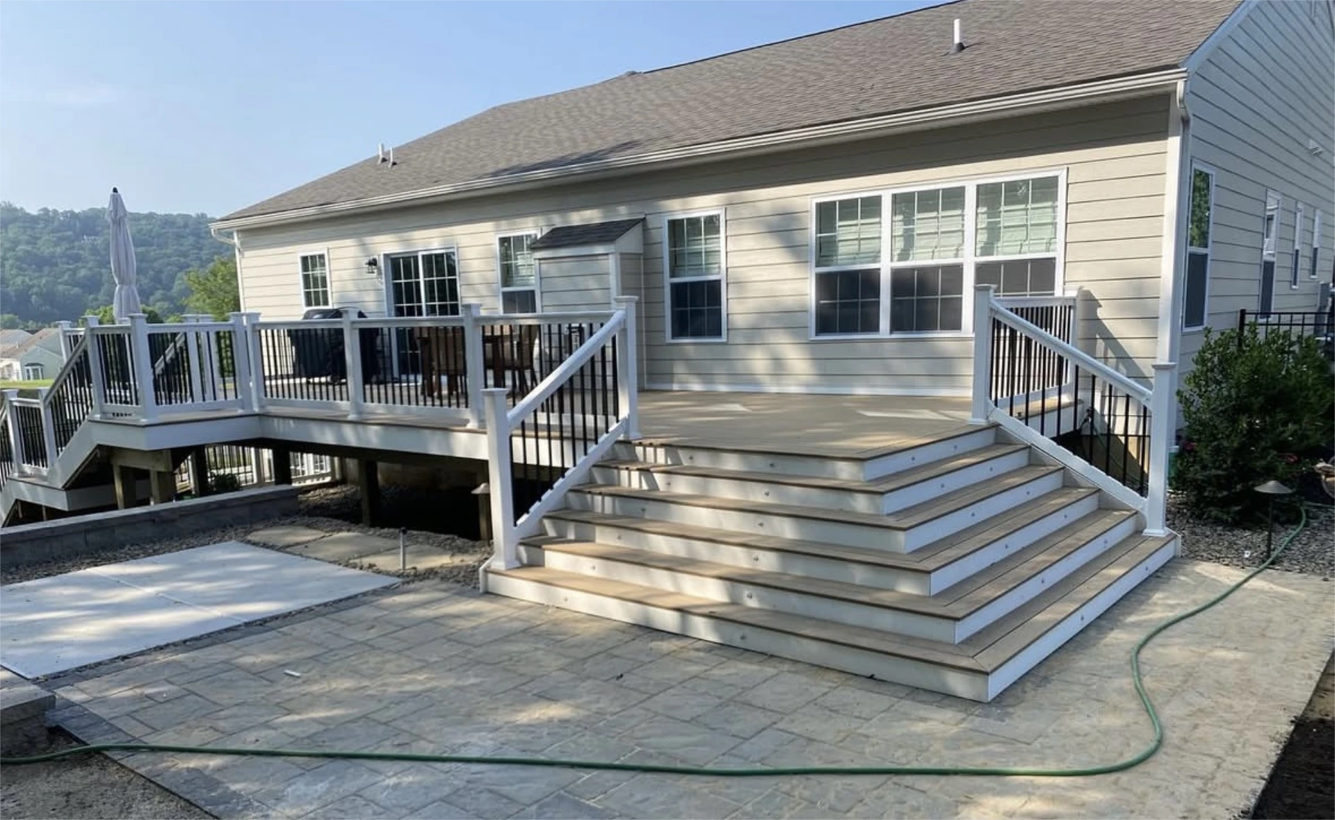 Elevated backyard deck with beige decking, white railings, and broad staircase over patio.