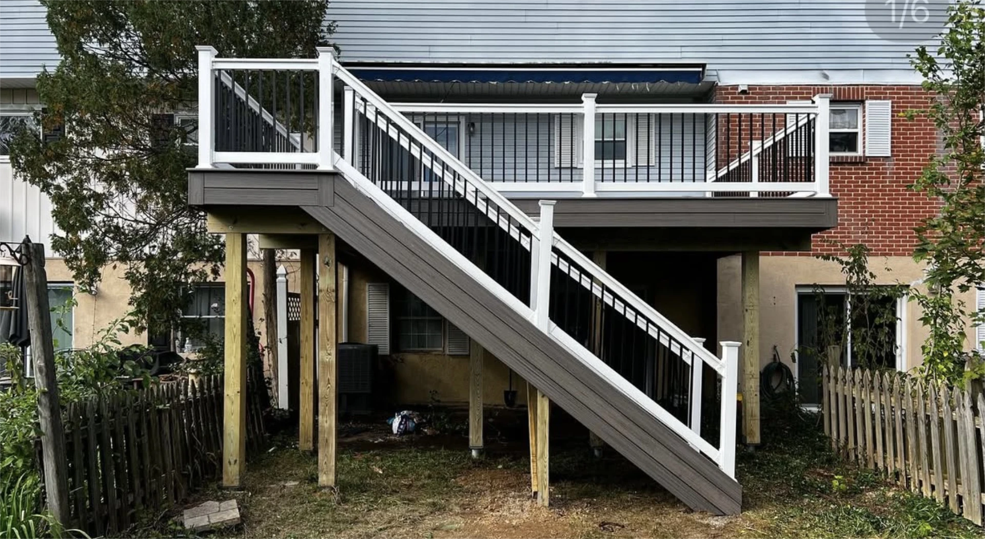 Elevated backyard deck with gray composite boards, white posts, black metal railings, and long staircase.