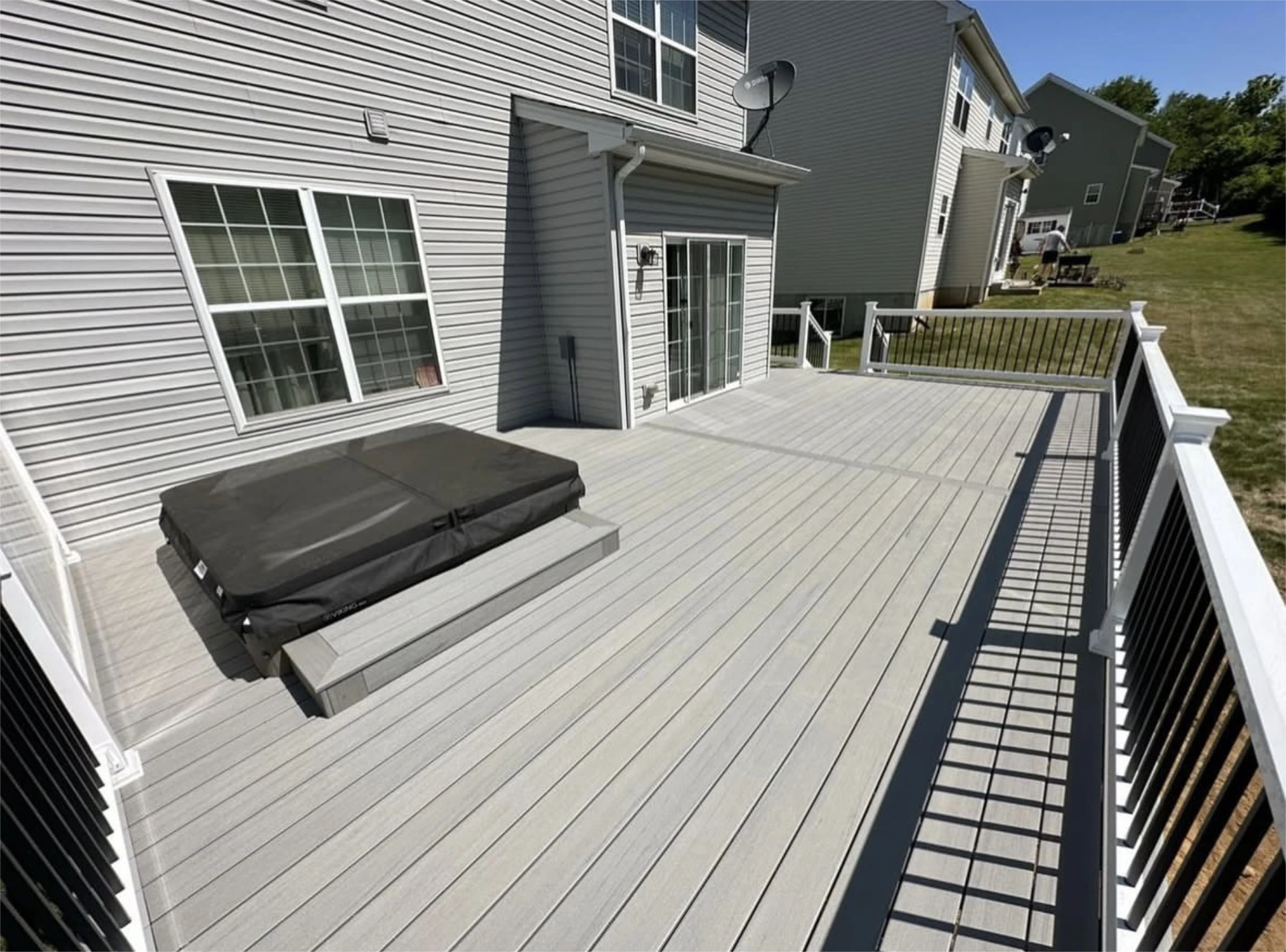 Elevated backyard deck with hot tub, sliding glass door, and black metal railing on a sunny day.