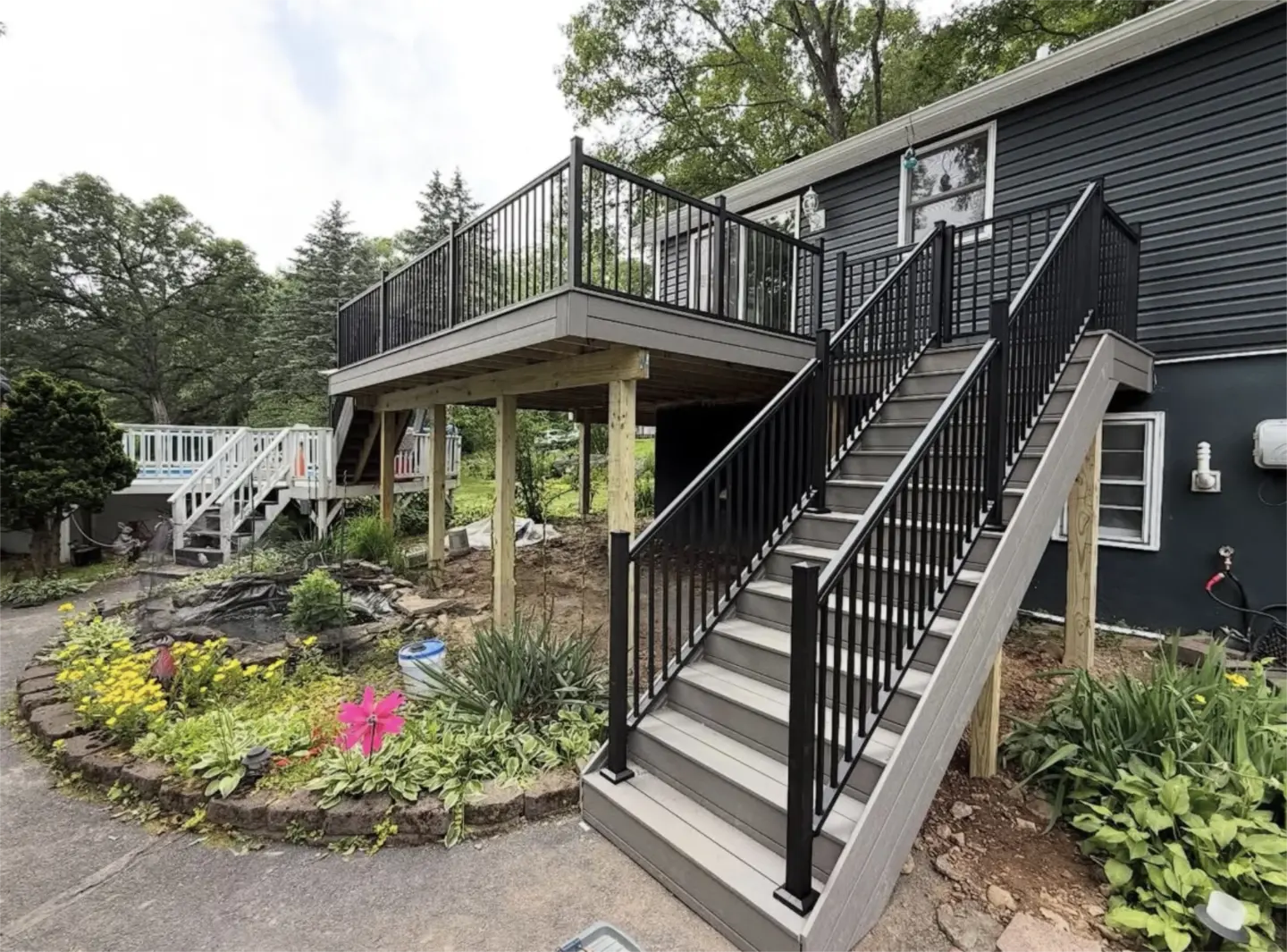 Elevated gray composite deck with black railings and dual staircases beside a dark sided home.