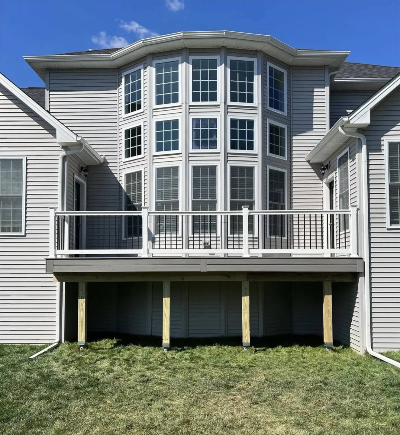 Elevated gray deck with white railing behind suburban home.