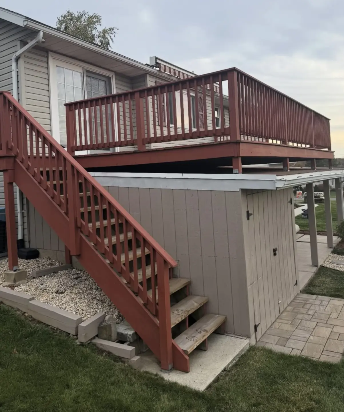 Elevated red wooden deck with stairs and railing beside house.