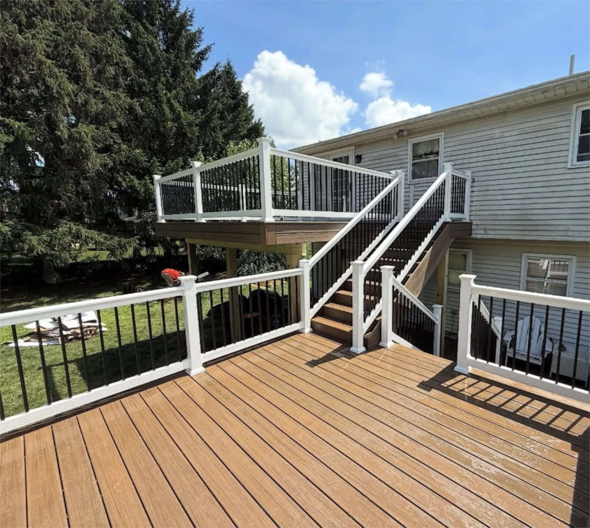 Elevated wood deck with white and black railing and central staircase beside a house.