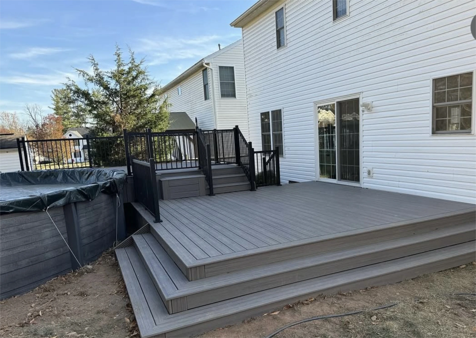 Gray composite backyard deck with stairs, black railing, and covered hot tub.