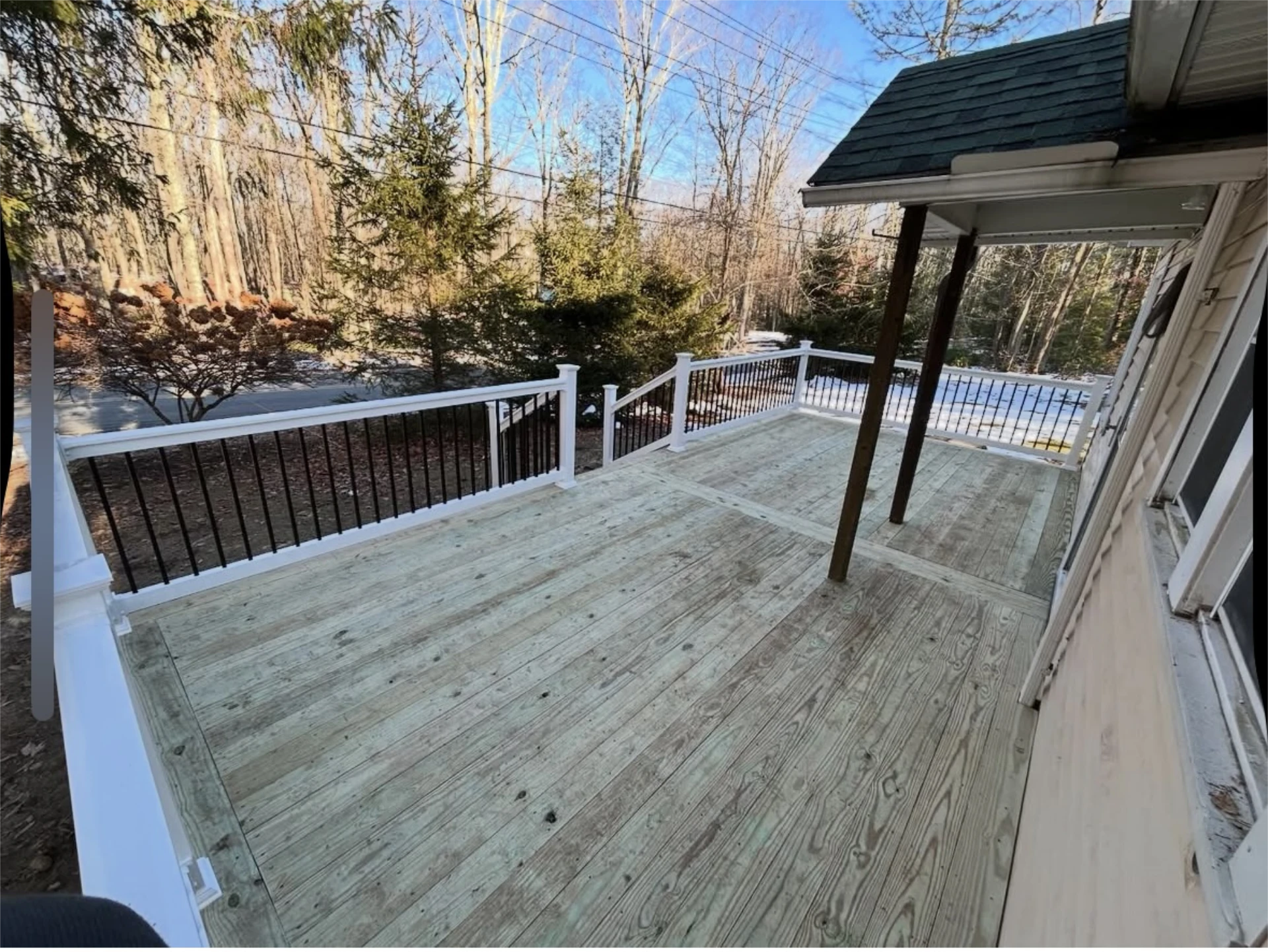 Large backyard deck with white railing and wooded view.