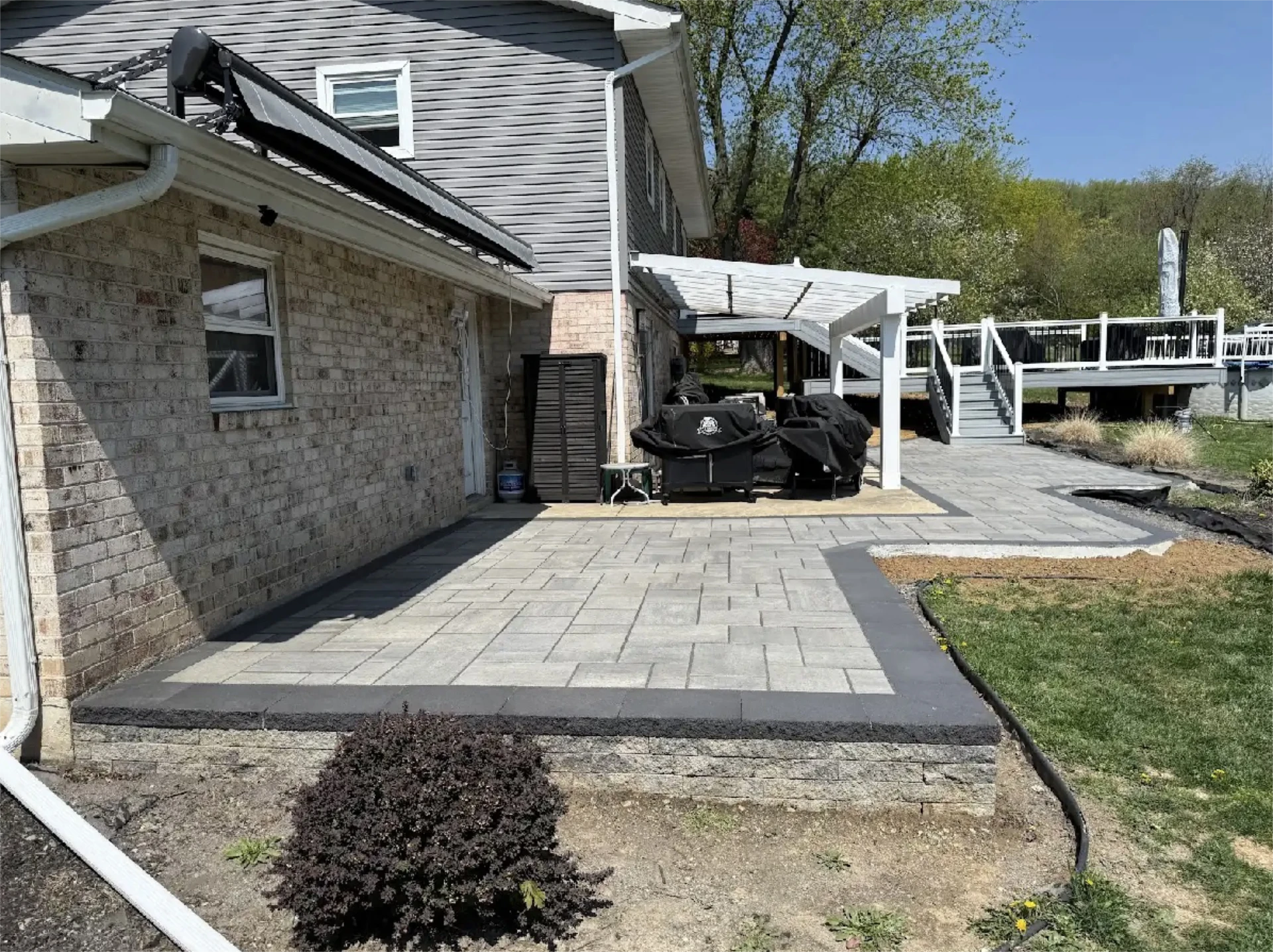 Large backyard patio with pergola, deck stairs, and stone pavers.
