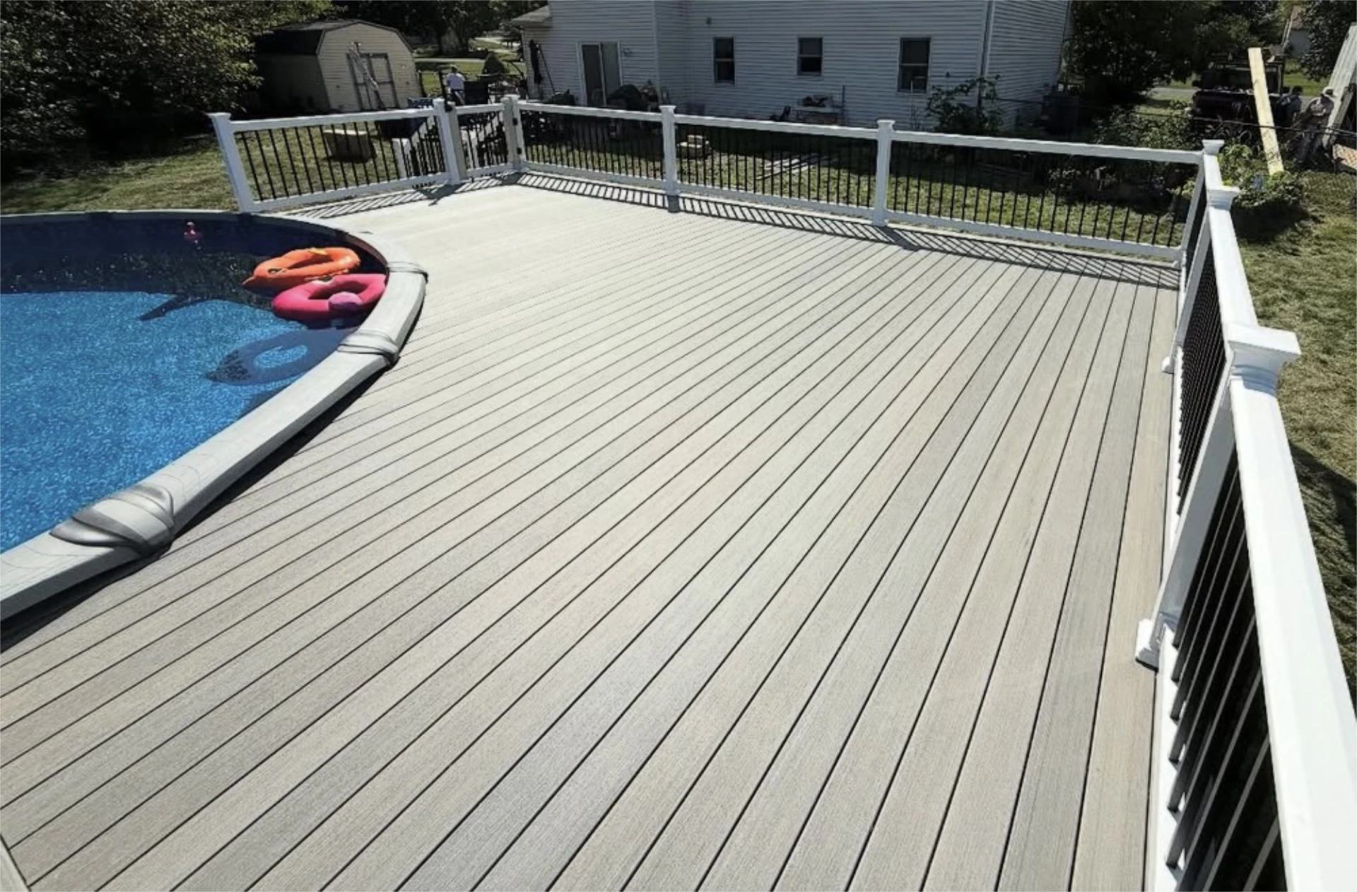 Large composite deck surrounding an above ground pool with white and black railing.