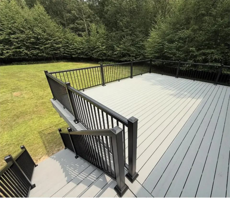 Large gray composite deck with black railing overlooking a grassy backyard and trees.