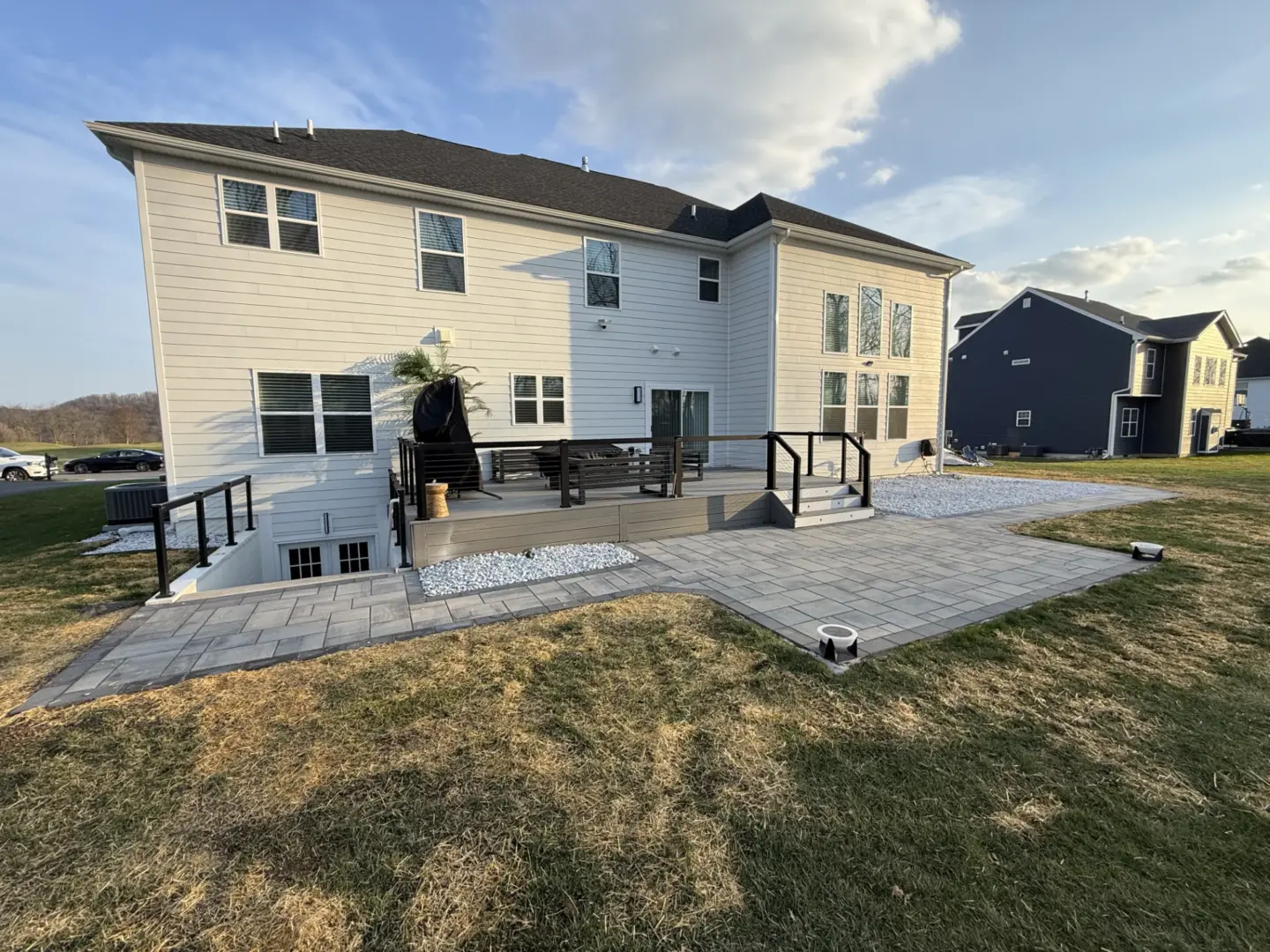 Large modern backyard patio with raised deck and wide paver terrace.