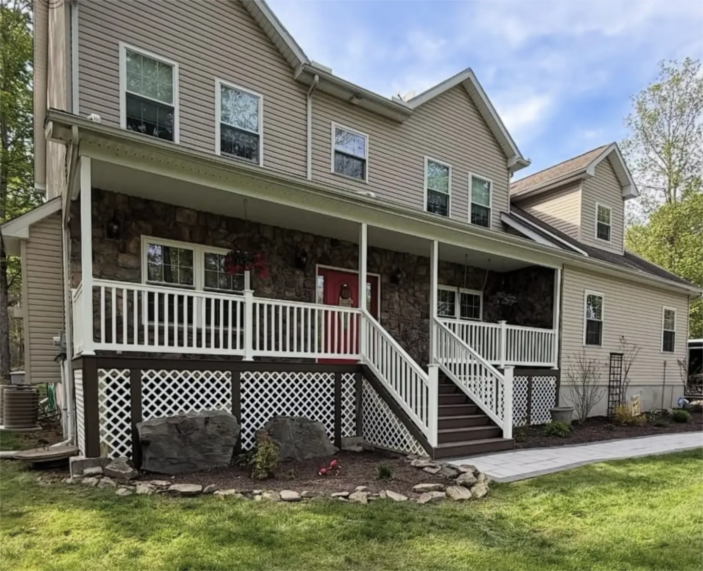Large two story home with wraparound porch, white railings, and landscaped front yard.