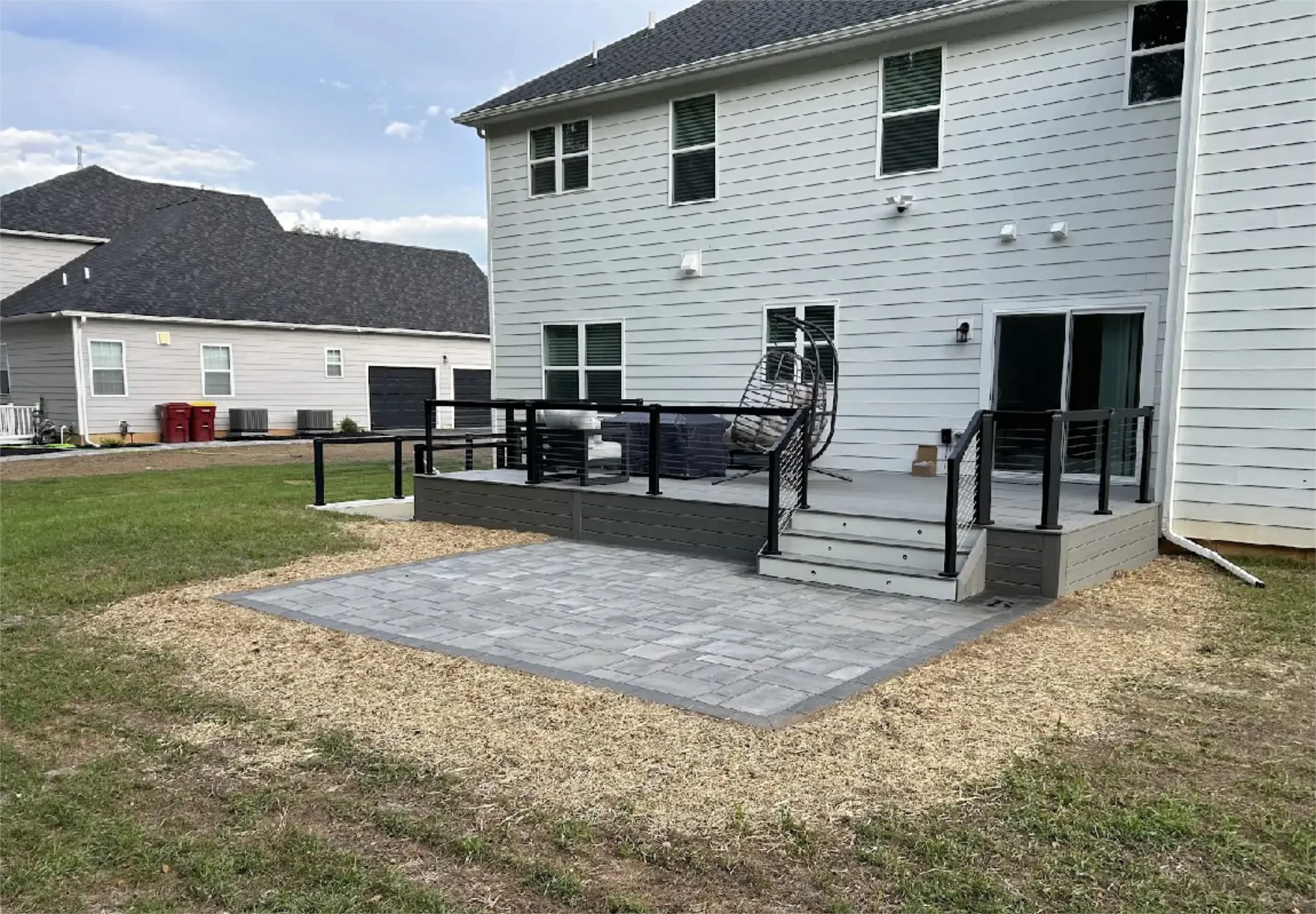Modern backyard deck with black railing and paver patio.