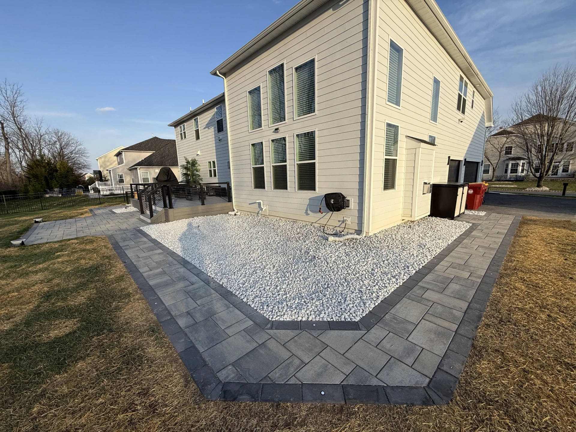 Modern backyard patio with white rock landscaping and gray pavers around a two story house.