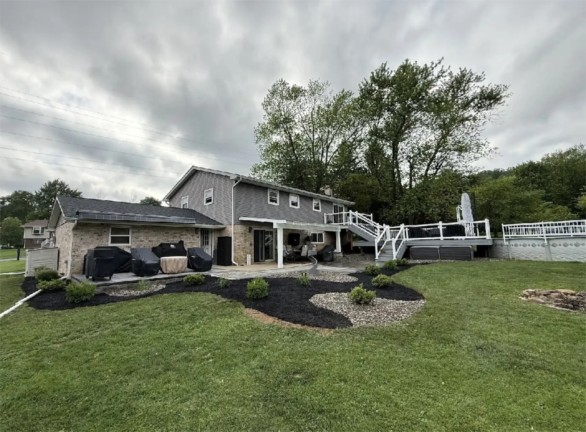 Modern backyard with raised deck, pergola patio, and landscaped lawn under cloudy sky.
