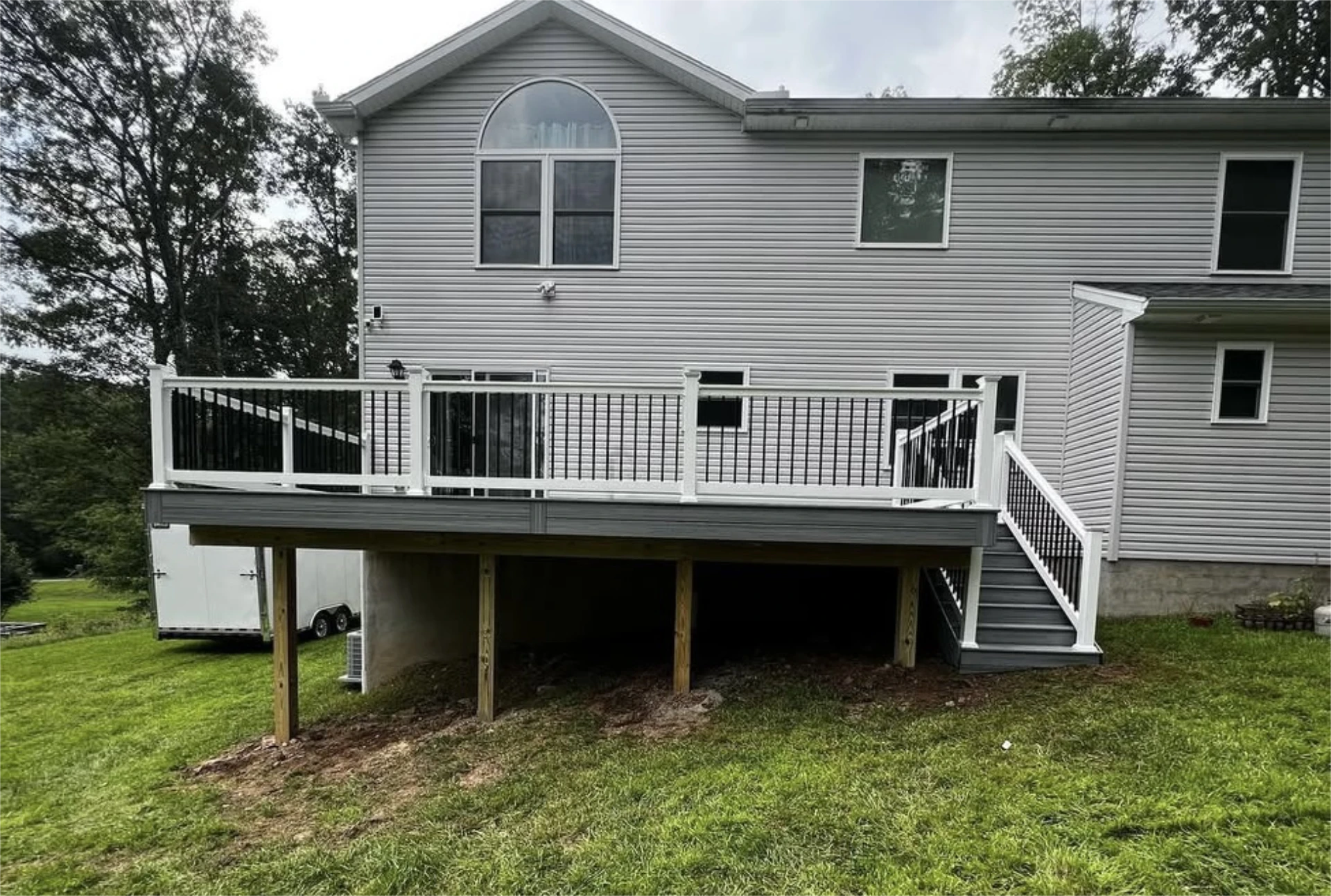 Modern elevated deck with white railing and stairs behind gray house.