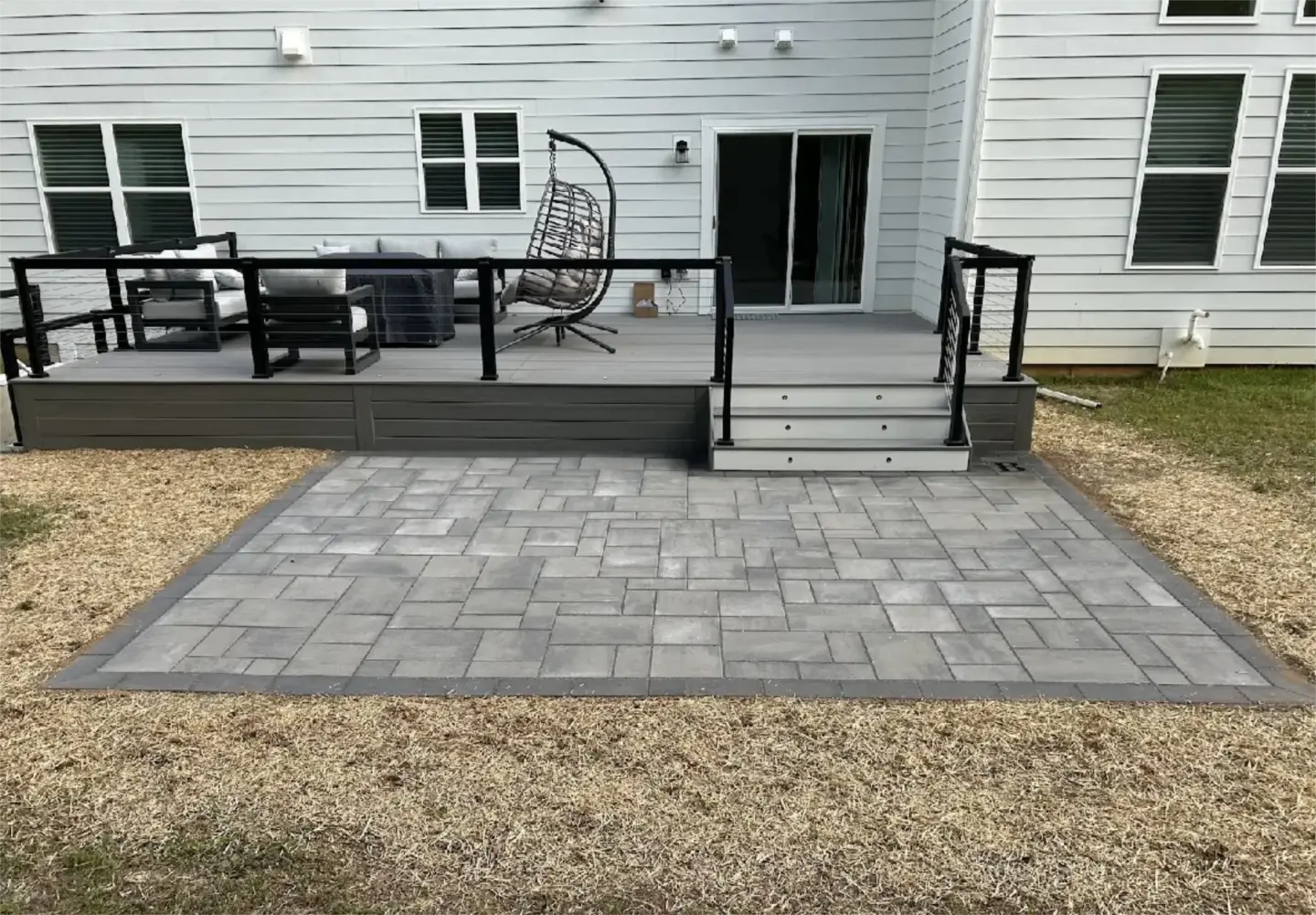 Modern gray paver patio with deck and stairs.
