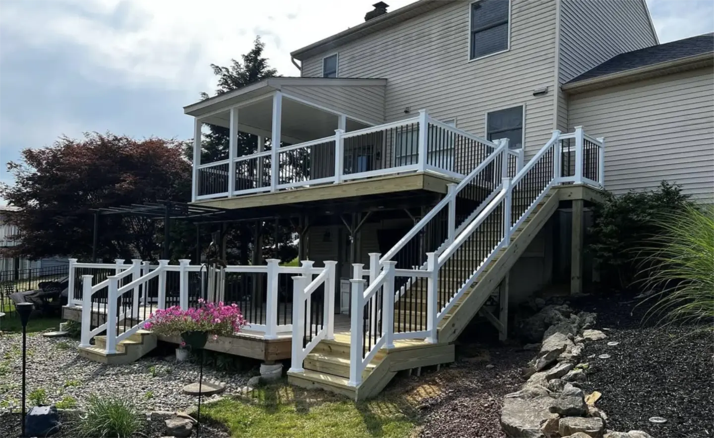 Multi level backyard deck with stairs, white posts, and black balusters.