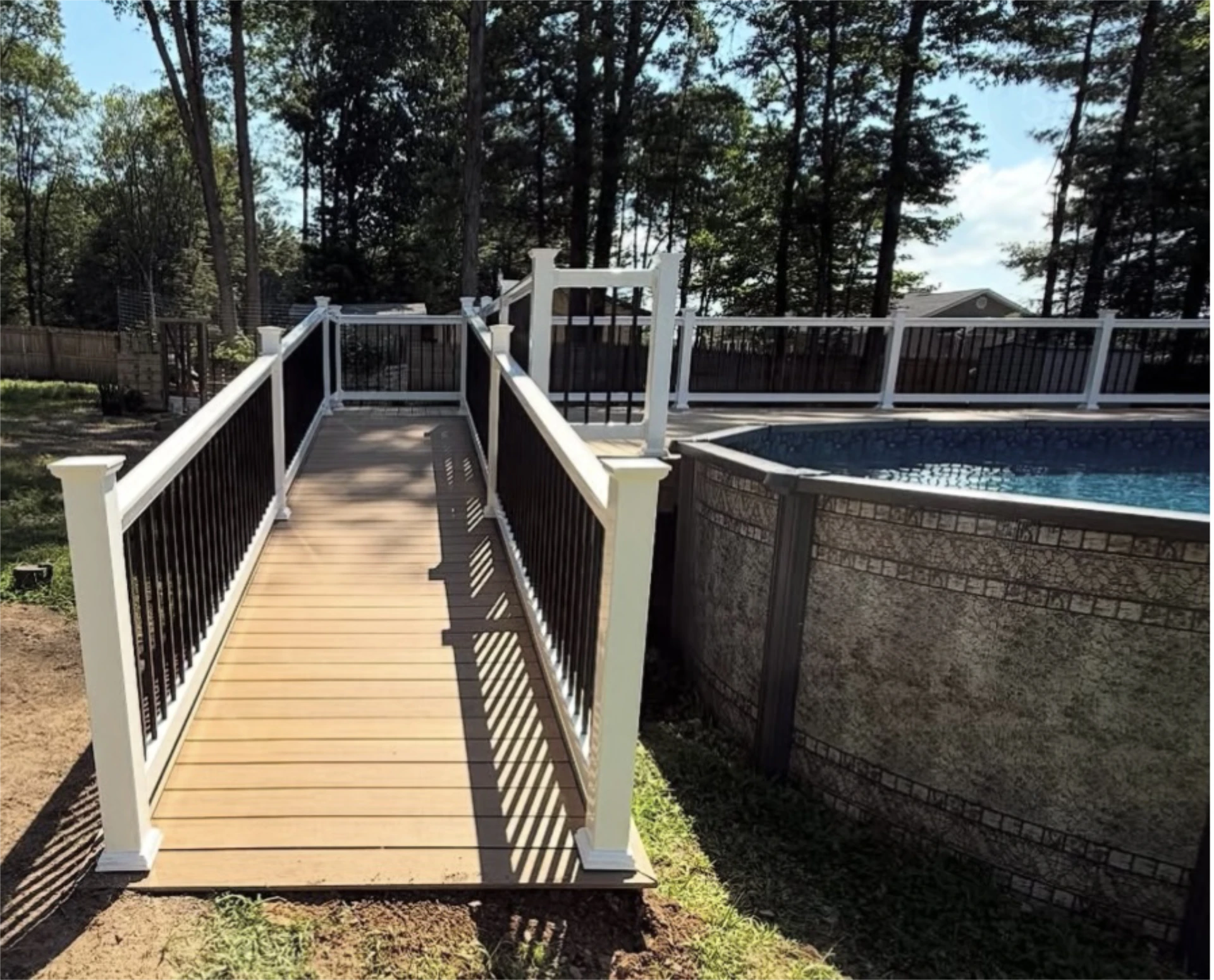 Narrow poolside walkway deck with white posts and black balusters beside an above ground pool.
