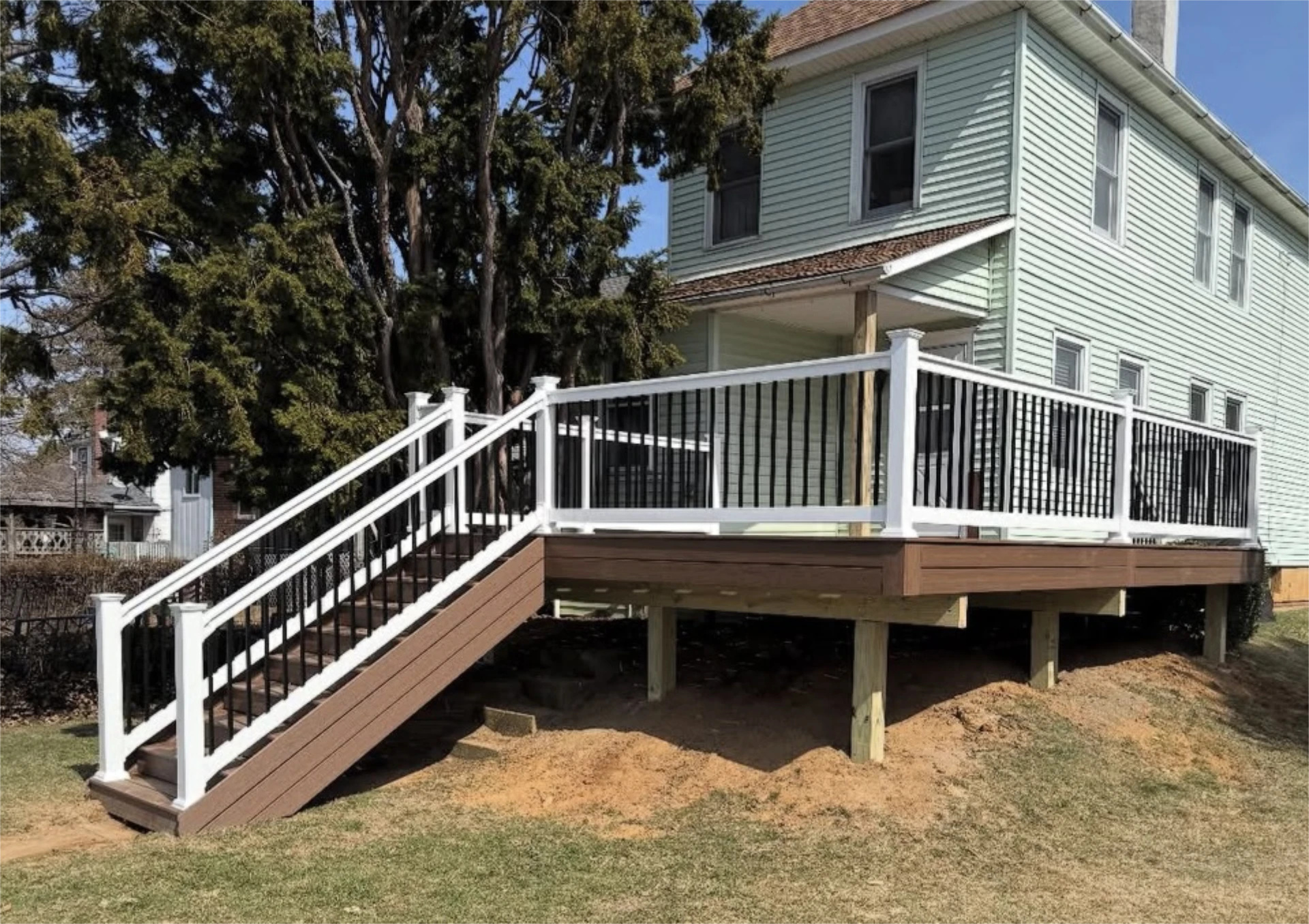 Raised composite deck with white railings and stairs beside a green house.