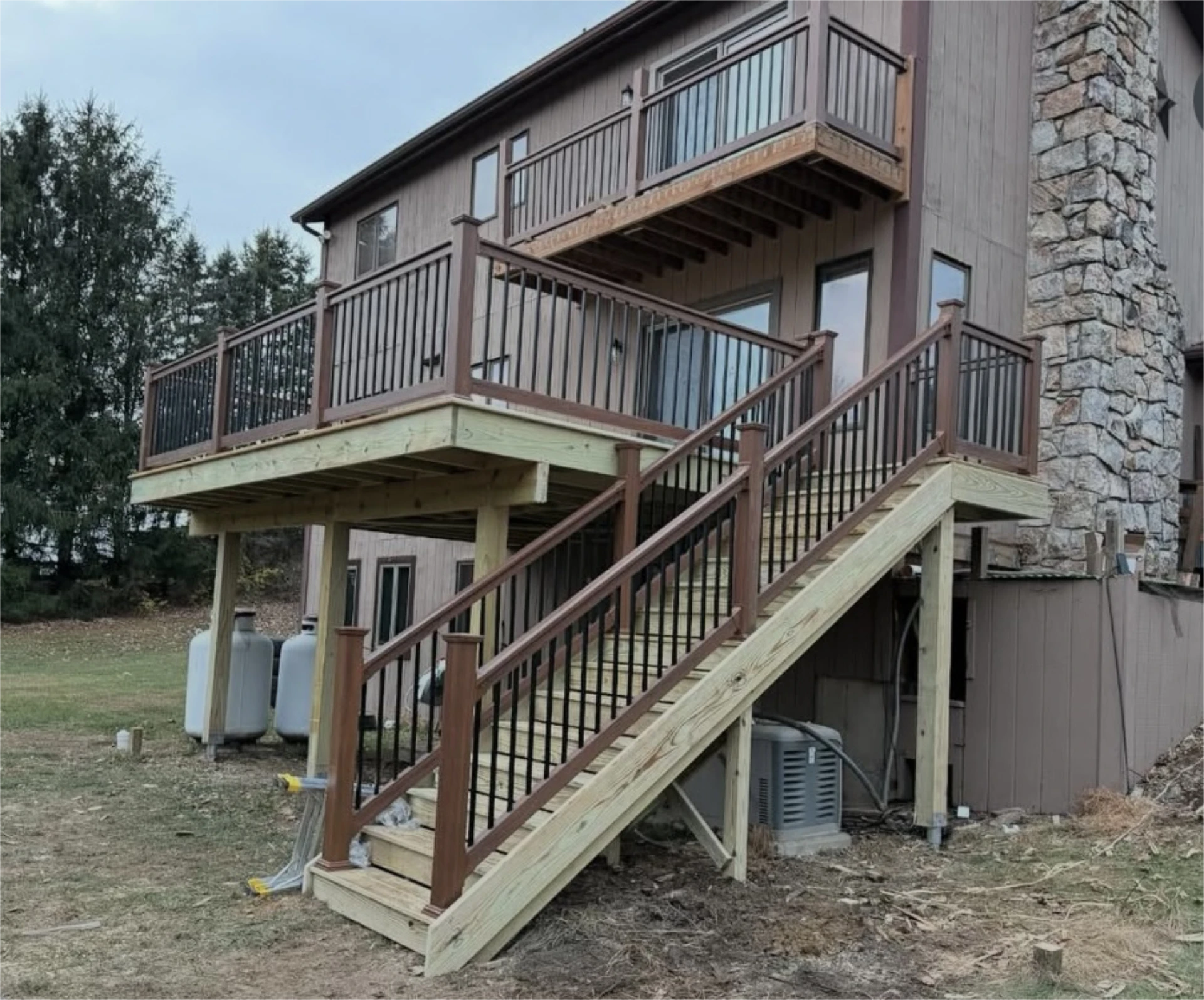 Raised deck with brown railings and long staircase beside house.