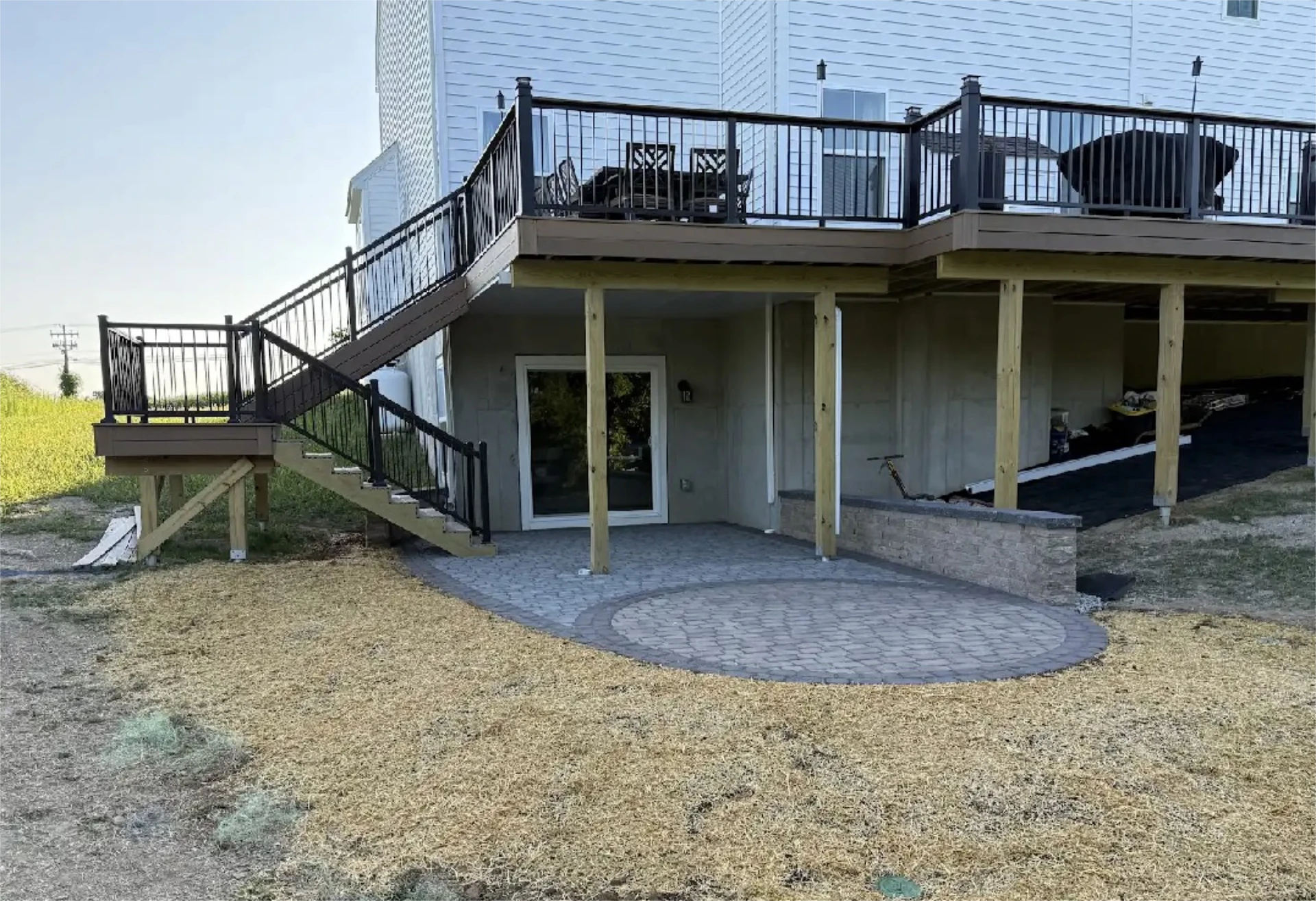 Raised deck with stairs leading to a circular paver patio under the deck.