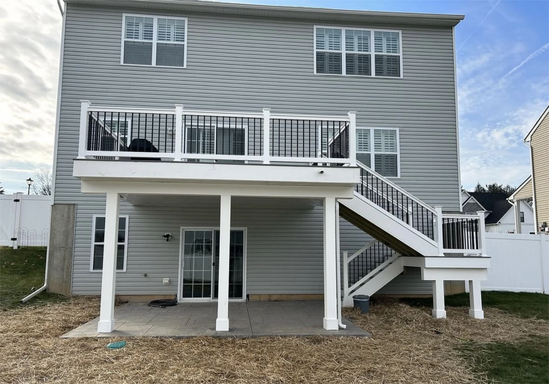 Rear view of two story home with elevated deck, covered patio, and staircase to backyard.
