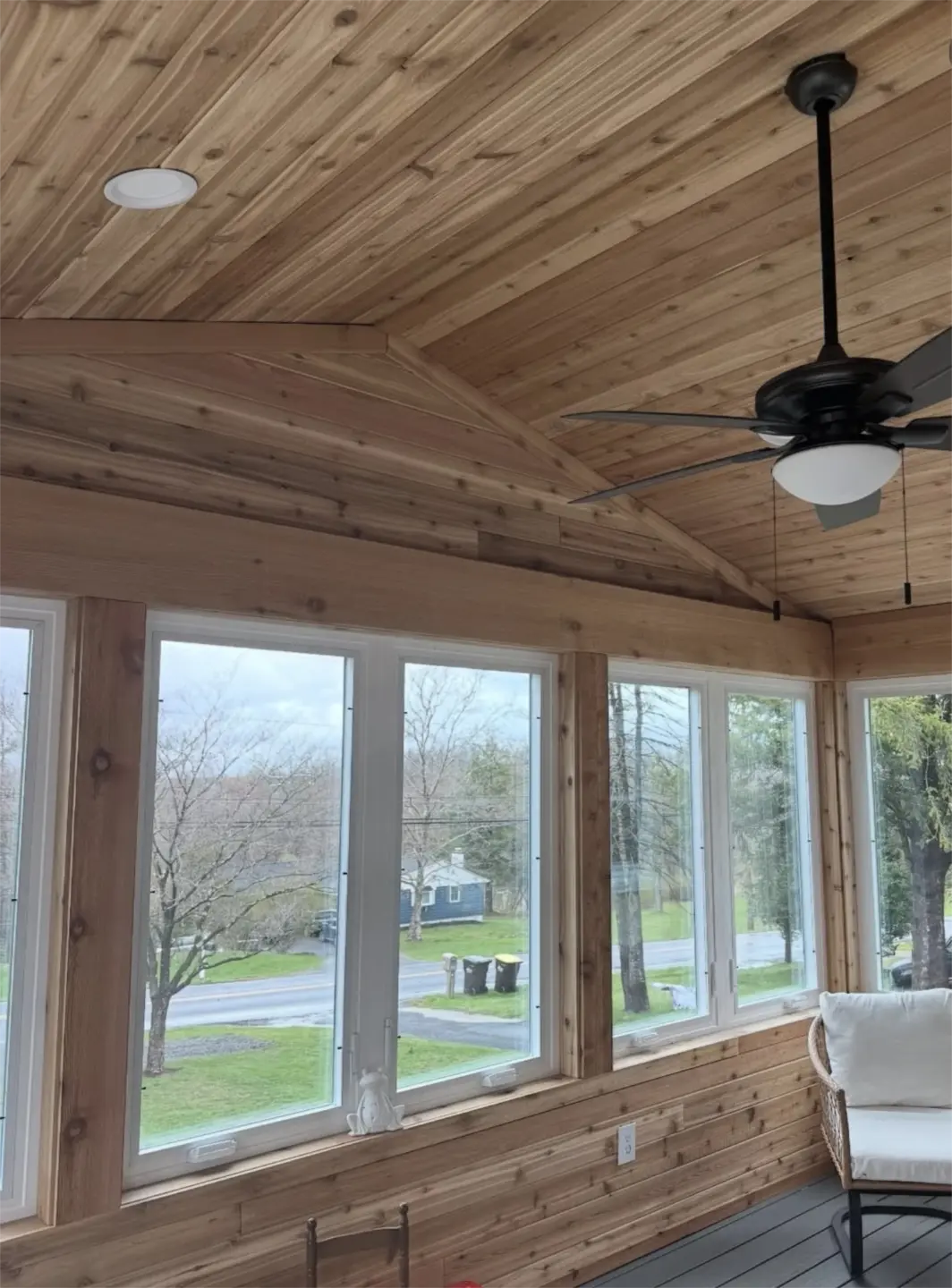 Rustic screened porch with vaulted wood ceiling and black ceiling fan.
