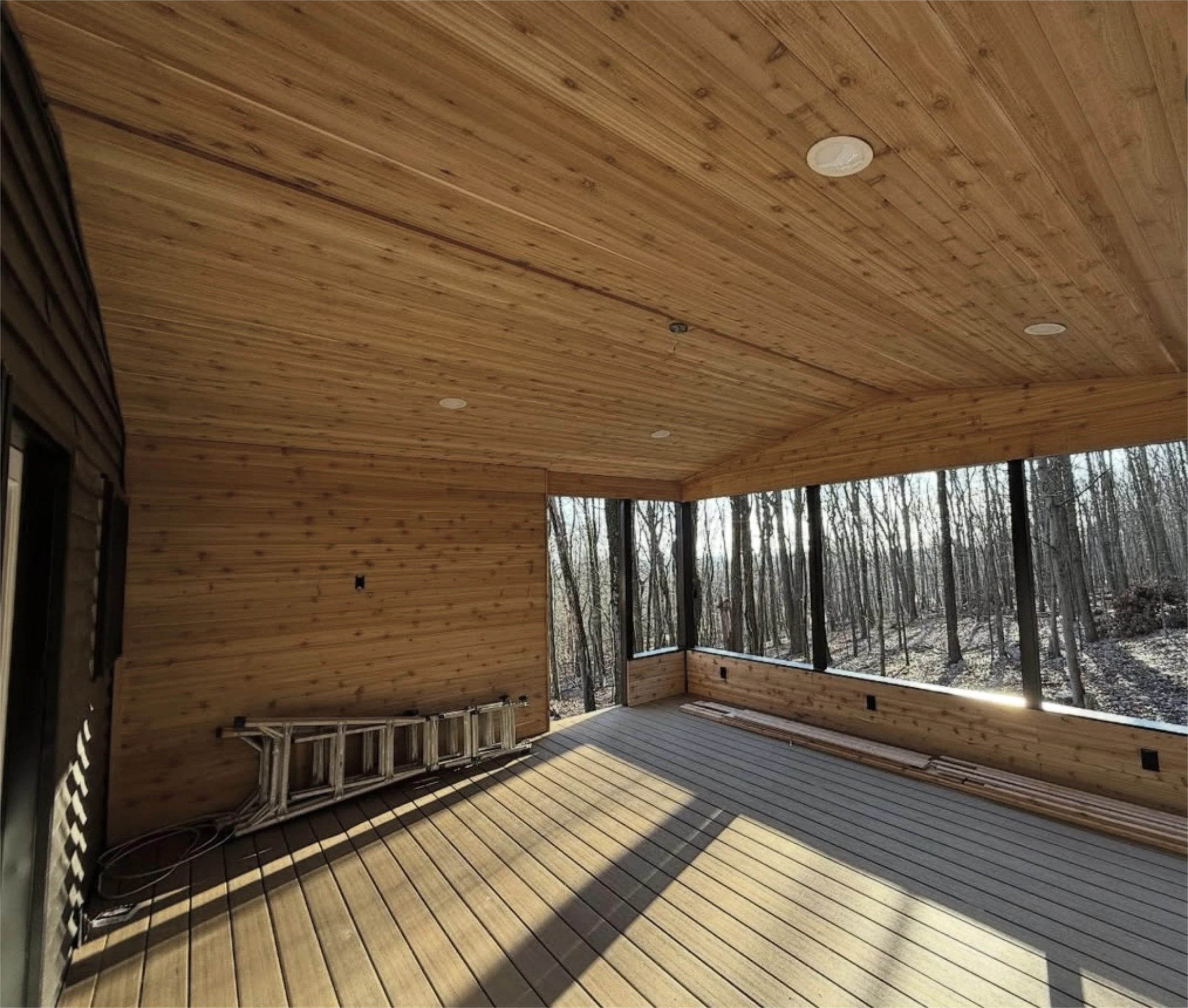 Screened porch with wood ceiling and forest view.