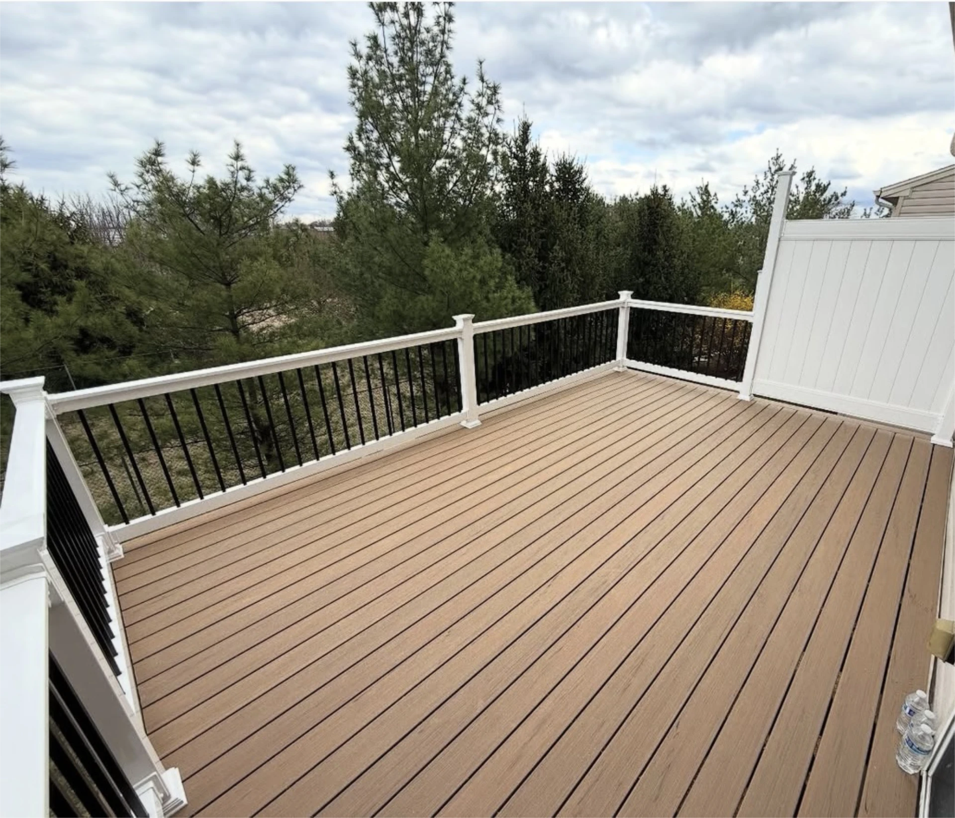Spacious elevated deck with white and black railing overlooking pine trees.
