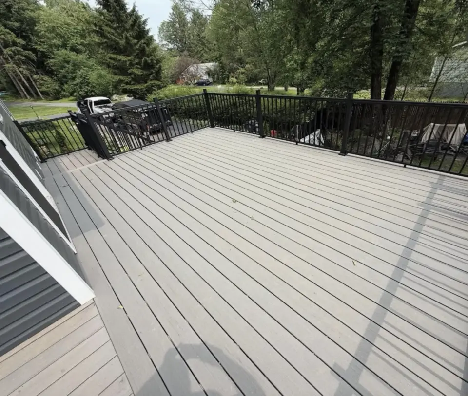 Spacious gray composite deck with black railings overlooking a wooded residential yard.