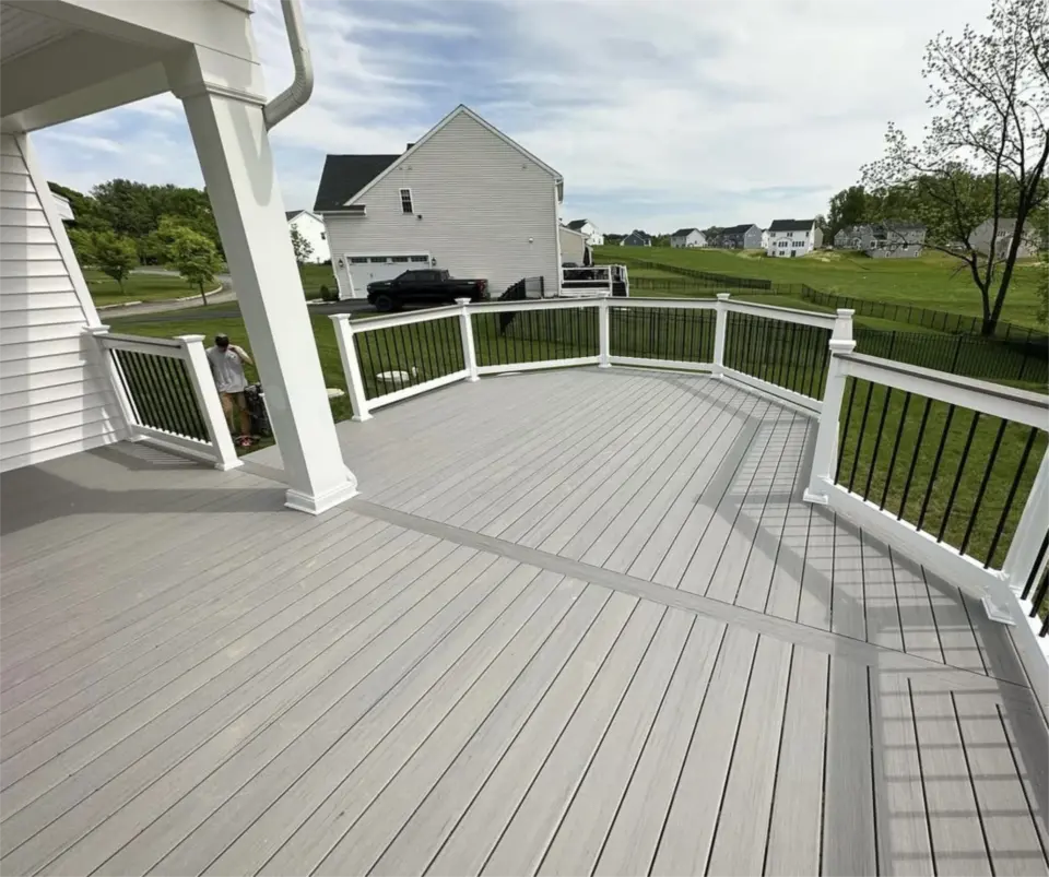 Spacious gray composite deck with white posts and black railings overlooking a suburban backyard.