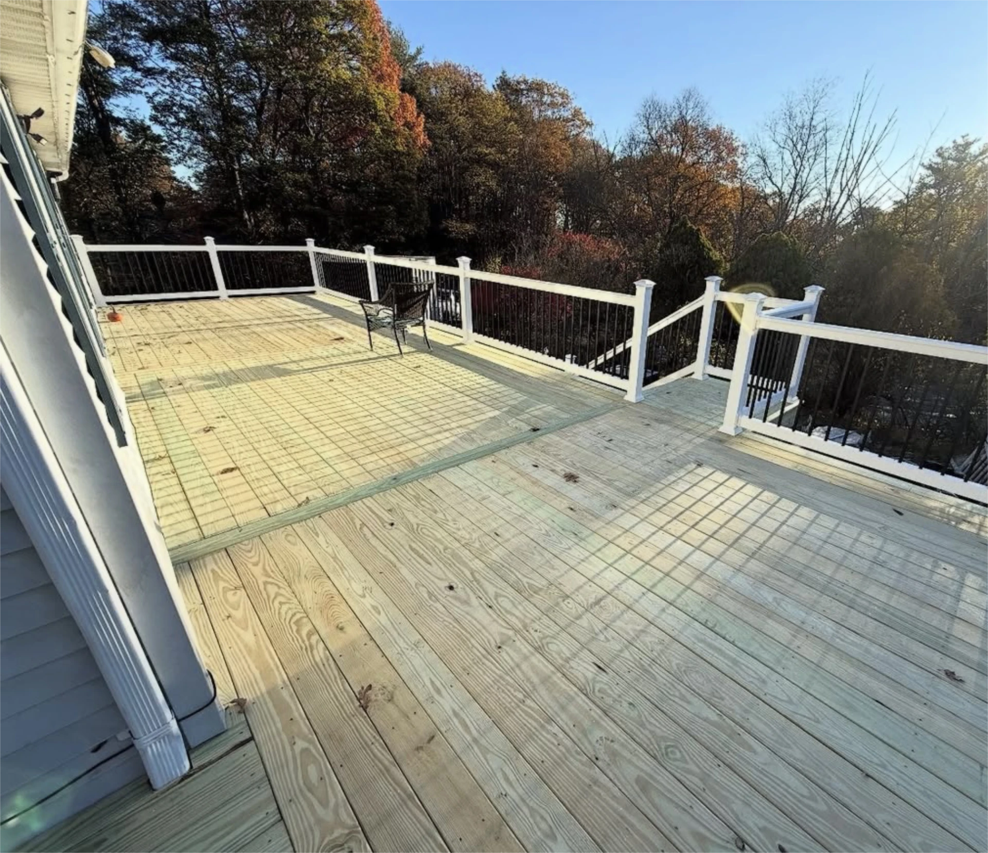 Spacious wood deck overlooking trees with black and white railing.