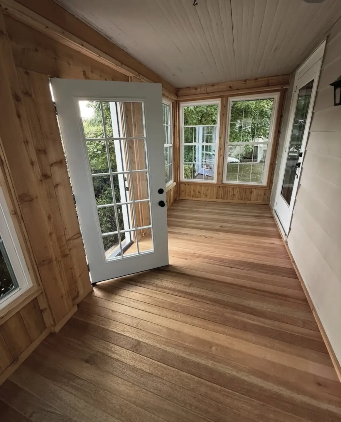 Sunlit enclosed porch with wood walls and glass door.