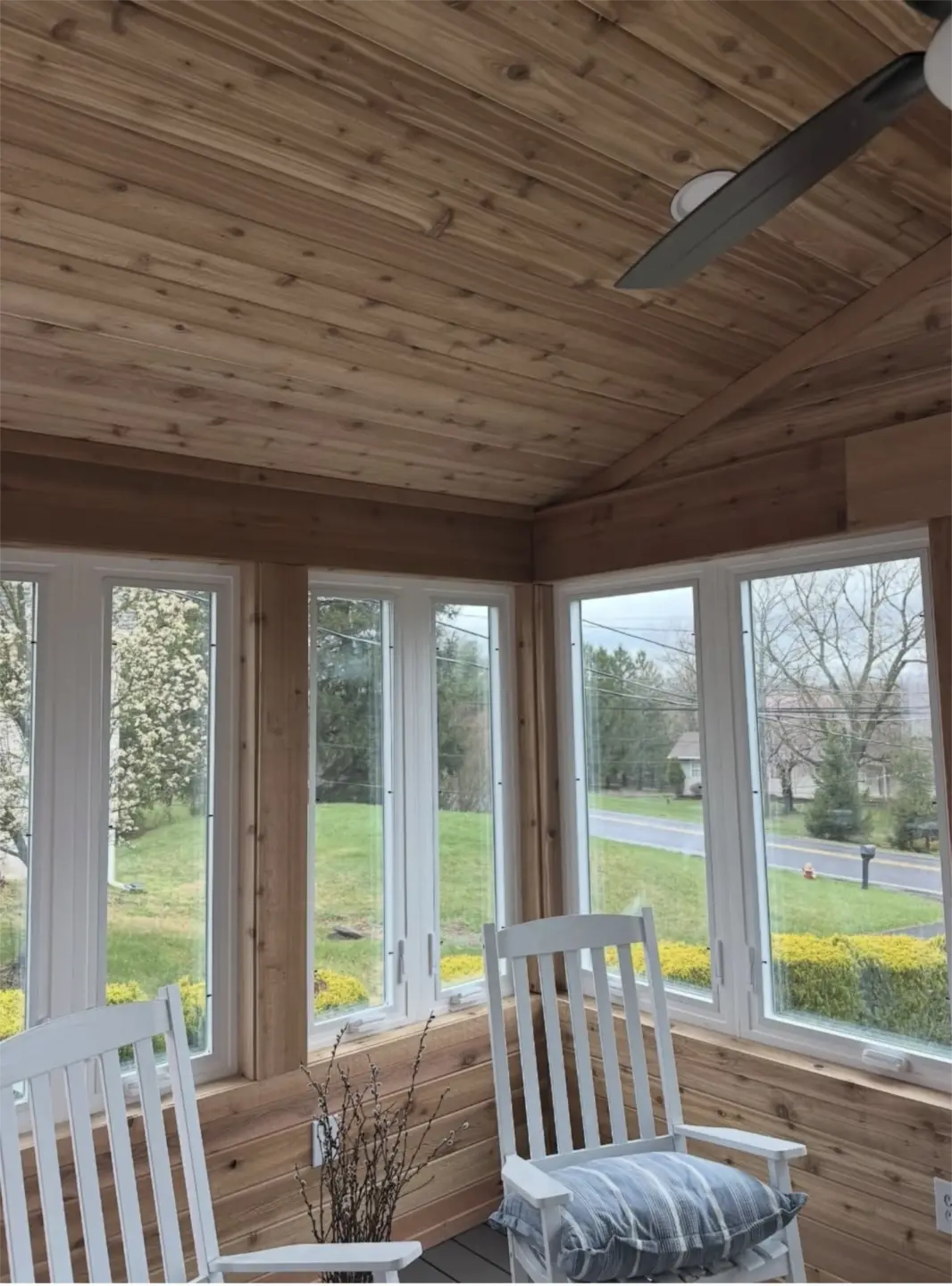 Sunroom with wood ceiling, large windows, and white rocking chairs.