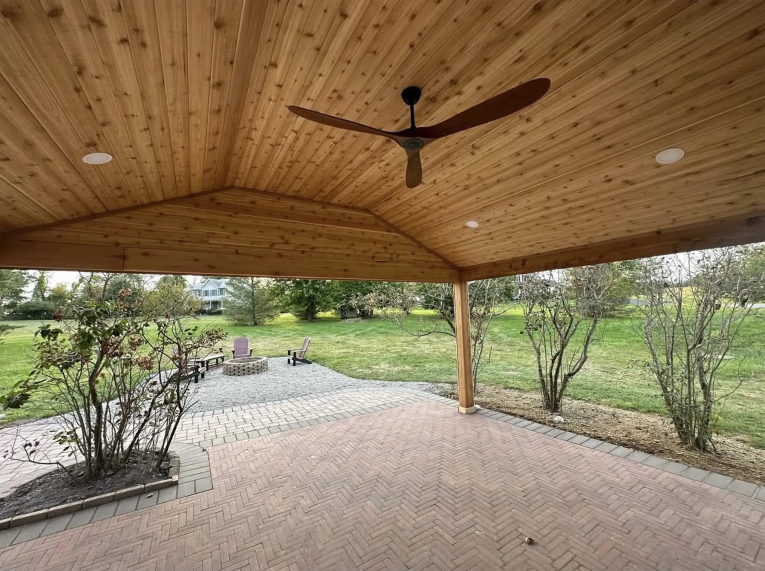 Wood paneled covered patio with ceiling fan and paver floor.